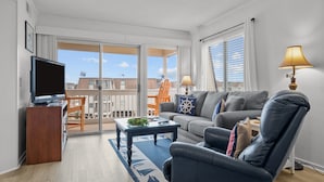 Una sala de estar moderna con sofá, sillón y mesa de centro, televisor y balcón con vistas.
