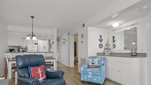Una sala moderna con un sillón de cuero y un sillón azul con motivos náuticos, una cocina con armarios blancos y una zona de comedor.