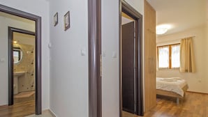 Ein Schlafzimmer mit Bett, einem Fenster mit Vorhängen und einem durch eine offene Tür einsehbaren Badezimmer.