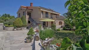 Ein zweistöckiges Haus mit Balkon, einer Treppe und einem Garten mit verschiedenen Pflanzen und Blumen.