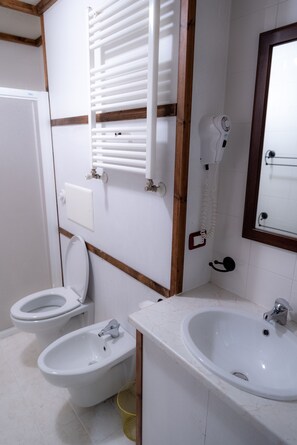 A bathroom with two toilets, a bidet, a sink, a mirror, and a towel rack. - Olimpo Sila Hotel (Taverna)