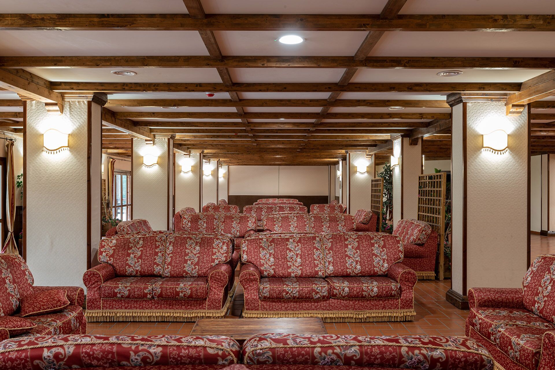 Un salón amplio con filas de sofás tapizados en rojo y vigas de madera en el techo.