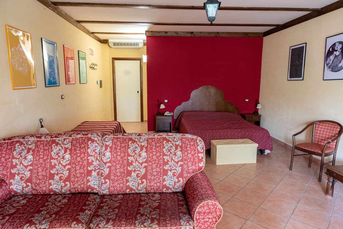 A hotel room with a red wall, a bed with a red and white checkered bedspread, a sofa with a floral pattern, and a chair.