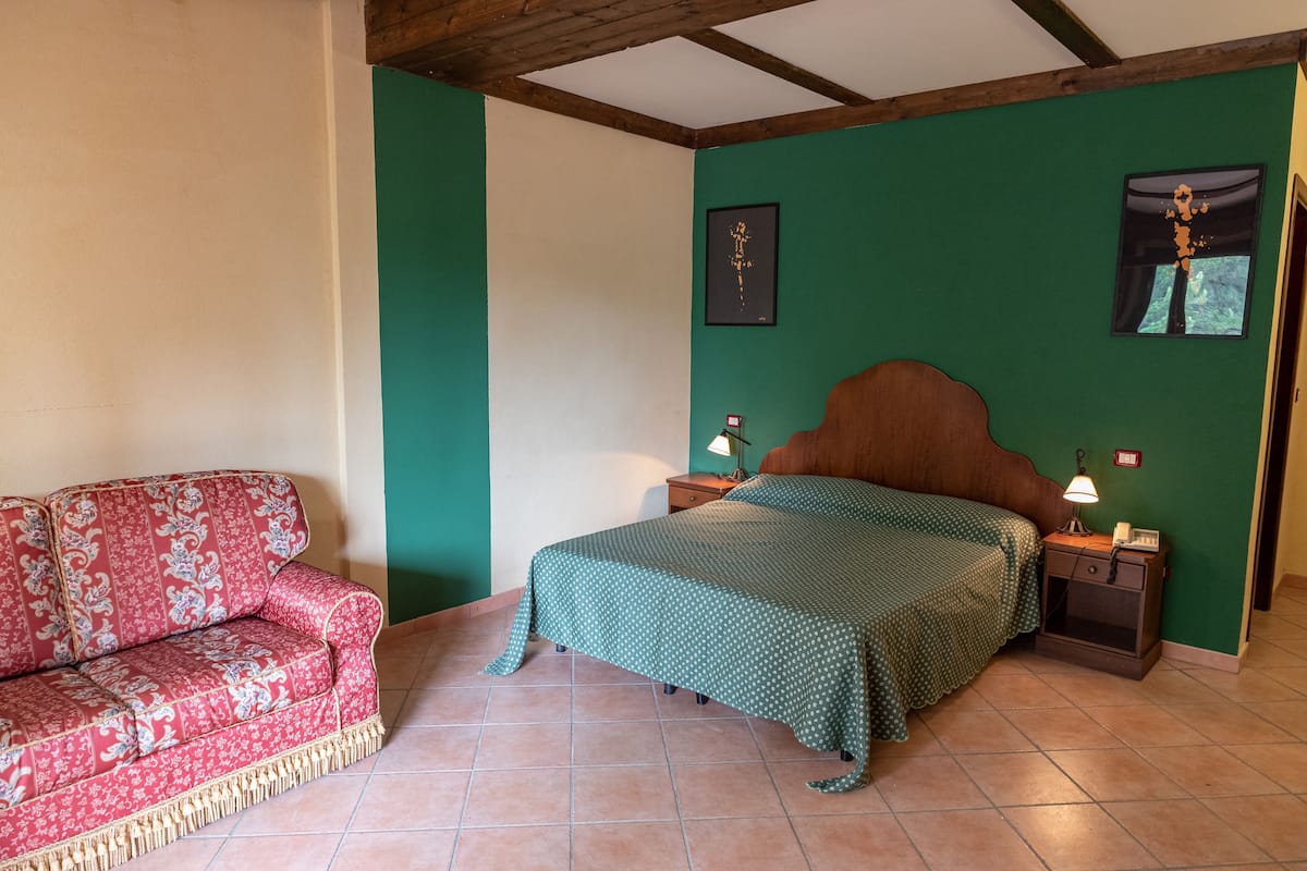 A bedroom with a bed, nightstands, a wooden headboard, a red patterned sofa, and green walls.