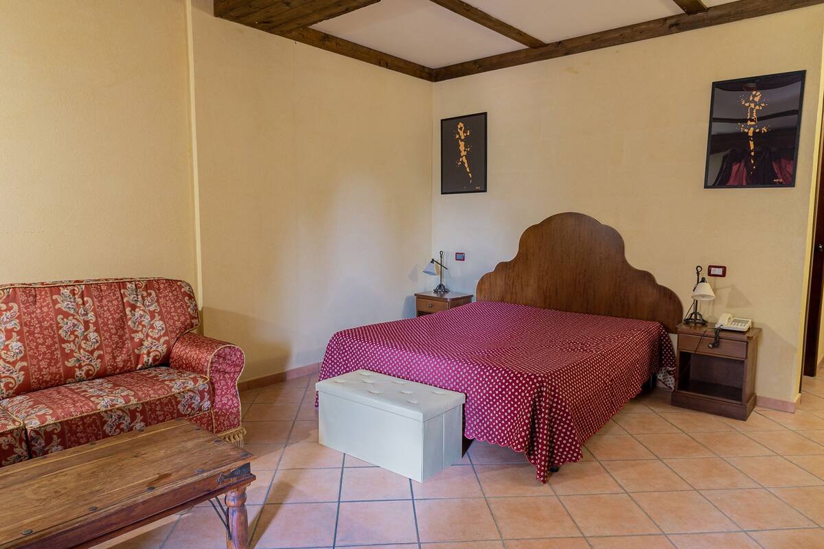 A bedroom with a bed, a nightstand, a lamp, a sofa, and a small table.