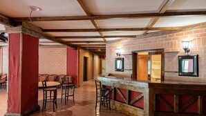 A rustic interior with exposed wooden beams, a brick wall, and a bar area with stools. - Olimpo Sila Hotel (Taverna)