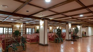 A spacious hall with high wooden beams, red patterned sofas, and potted plants. - Olimpo Sila Hotel (Taverna)