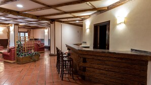 A rustic interior with exposed wooden beams, a tiled floor, a wooden reception desk, and a seating area with chairs and a sofa. - Olimpo Sila Hotel (Taverna)