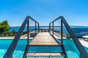 A wooden deck leading to a pool with a clear view of the sea and distant mountains. - Seaview Villa Blue Lagoon with private heated pool, 2 jacuzzies, sauna, media room, 6 bedrooms, beach 70m (Pisak)