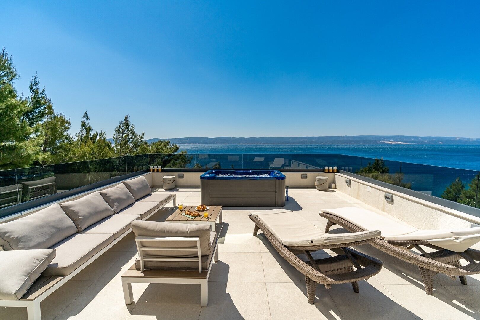 Terraço no telhado com sofás, poltronas de descanso e banheira de hidromassagem, com vista para a costa.