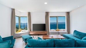 A modern living room with a large flat-screen TV, teal sofas, and a wooden coffee table. - Seaview Villa Blue Lagoon with private heated pool, 2 jacuzzies, sauna, media room, 6 bedrooms, beach 70m (Pisak)