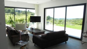 A spacious living room with a large TV, comfortable seating, and a view of a lush landscape through large windows. - Villa Exceptionnelle , Avec vue Panoramique (Venasque)