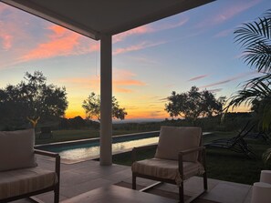 Ein überdachter Außenbereich mit Blick auf ein Schwimmbecken und den Sonnenuntergang.