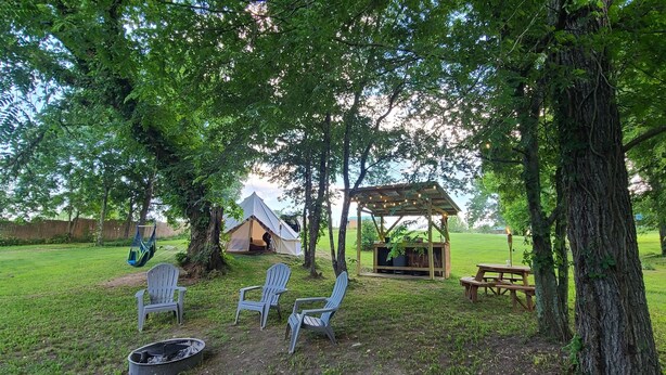 A tented camping area with a picnic table, chairs, and a fire pit. - Kings River Bell Tent Glamping  (Eureka Springs)