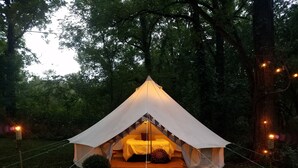 A tent with a bed inside, surrounded by trees and lit by string lights. - Kings River Bell Tent Glamping  (Eureka Springs)