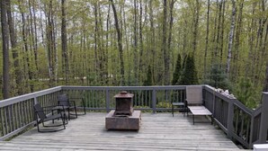 Une terrasse en bois avec un foyer et un espace salon, le tout entouré d’arbres.