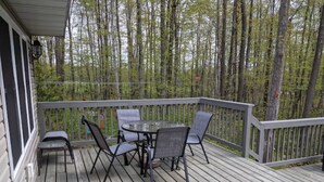 Une terrasse en bois, agrémentée d’une table et de chaises, entourée d’une rambarde et offrant une vue sur une zone boisée.
