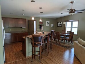 A spacious kitchen with wooden cabinets, a central island with bar stools, a dining area with a table and chairs, and a ceiling fan. - Secluded Home in Central Door County (Egg Harbor)