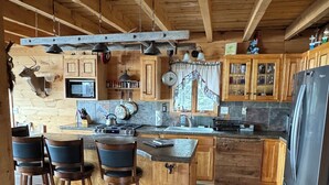 Une cuisine rustique avec des poutres en bois, un îlot central doté de tabourets de bar, un réfrigérateur et un four à micro-ondes.
