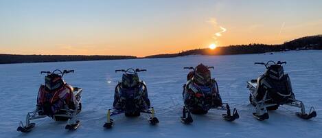 Quatre motoneiges sur un lac gelé, avec le soleil couchant en arrière-plan.