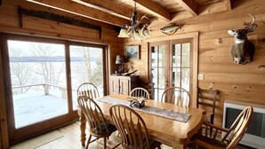 Une salle à manger en bois, avec une grande table et des chaises, un lustre et une tête de cerf accrochée au mur.