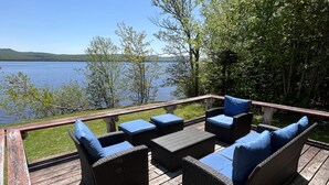 Une terrasse en bois, meublée de mobilier en osier, avec vue sur un lac.