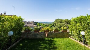 A garden with a stone wall, potted plants, and a view of a town in the distance. - San Gimignano Town Garden - 4 pax (San Gimignano)