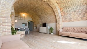 A spacious living area with a high arched brick ceiling, a modern sofa, a television, and a dining area with a table and chairs. - San Gimignano Town Garden - 4 pax (San Gimignano)