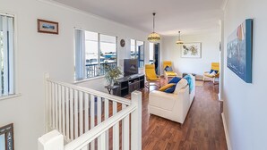 Een ruime woonkamer met een witte bank, een televisie en een balkon met uitzicht op zee.
