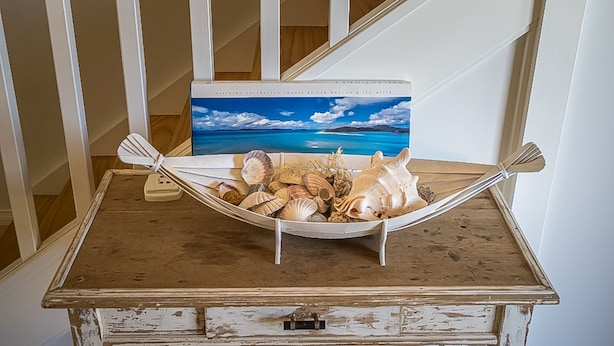 Een hangmat gevuld met schelpen op een houten tafel, met een schilderij van een strand in de achtergrond.