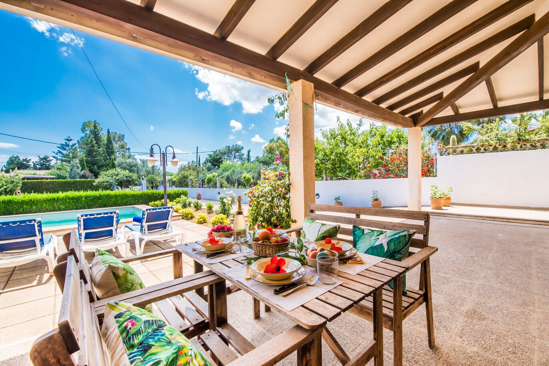 Un patio al aire libre con muebles de madera, piscina y vistas a un jardín.