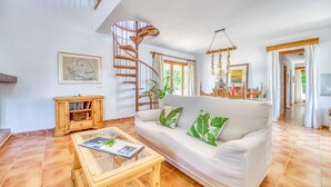 A spacious living room with a white sofa, a wooden coffee table, a spiral staircase, and a bookshelf. - Finca with pool Ca Na Tonina in Puerto Pollensa (Puerto Pollensa)