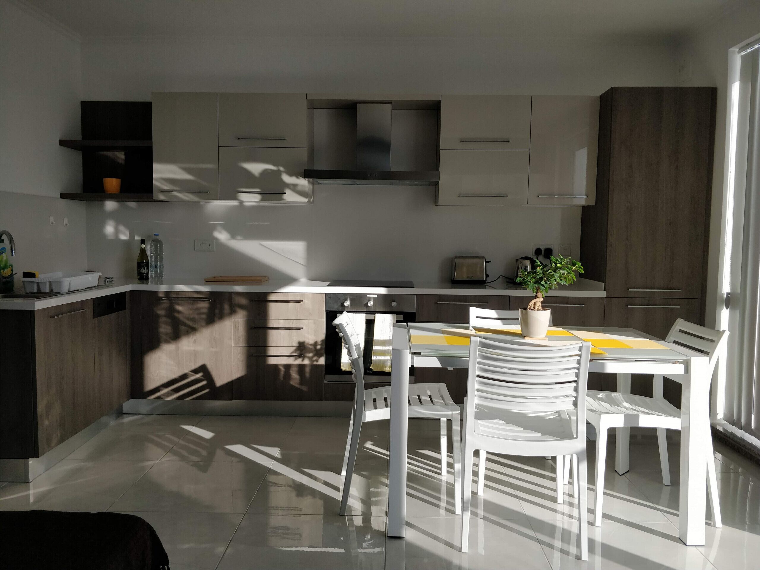 Une cuisine moderne avec des meubles blancs, un îlot central et un coin repas avec des chaises blanches.