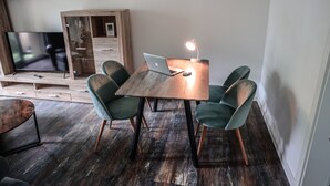 Ein modernes Wohnzimmer mit einem Holztv-Schrank, einem Esstisch mit einem Laptop und grünen Sesseln.