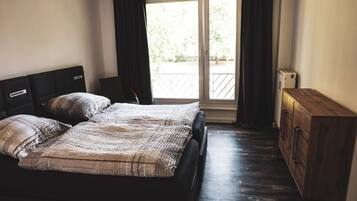 A bedroom with two beds, a wooden dresser, and a sliding glass door leading to a balcony.
