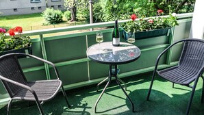 Ein Balkon mit zwei Korbstühlen, einem kleinen runden Tisch und einer Weinflasche.
