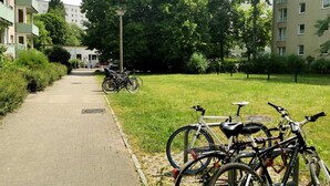 Ein gepflasterter Weg in einer Wohngegend, auf dem Fahrräder auf dem Rasen abgestellt sind.