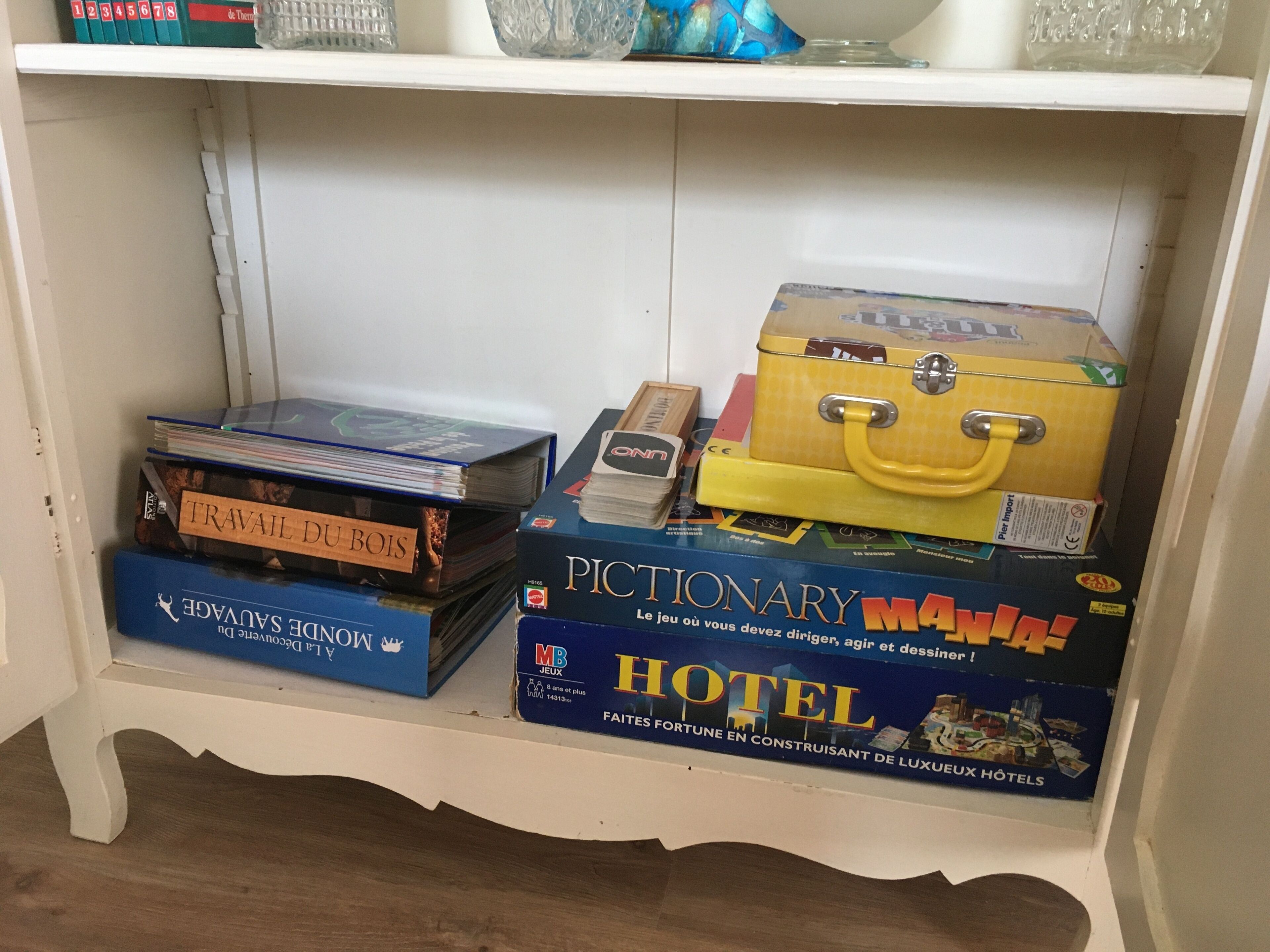Une étagère contenant divers jeux de société, notamment « TRAVAIL DU BOIS » et « PICTIONARY MAIN ».