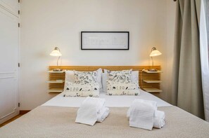 A neatly made bed with two pillows, a framed picture on the wall, and bedside lamps.