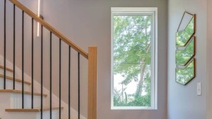 Eine moderne Treppe mit Holzboden und schwarzen Geländern, die zu einer Empore mit einem großen Fenster und Blick auf Bäume führt.