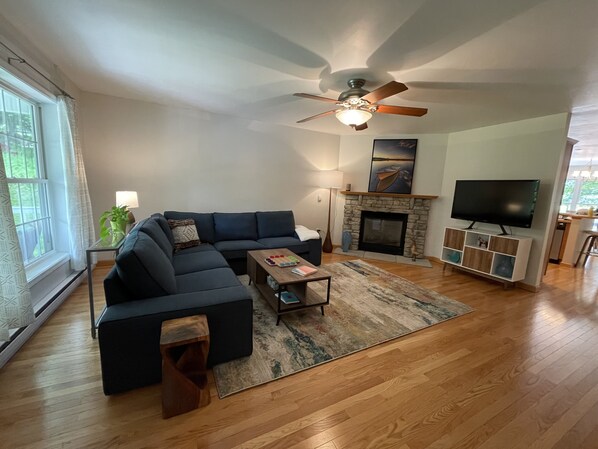 Una sala de estar moderna con un sofá modular, chimenea, televisor y ventilador de techo.