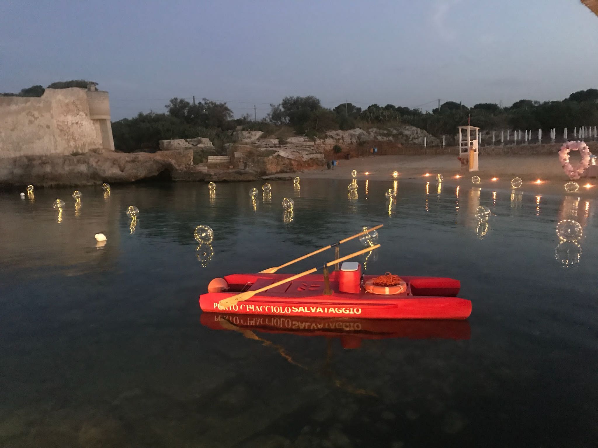 A red boat with oars and life jackets on a calm body of water, surrounded by rocks and trees.