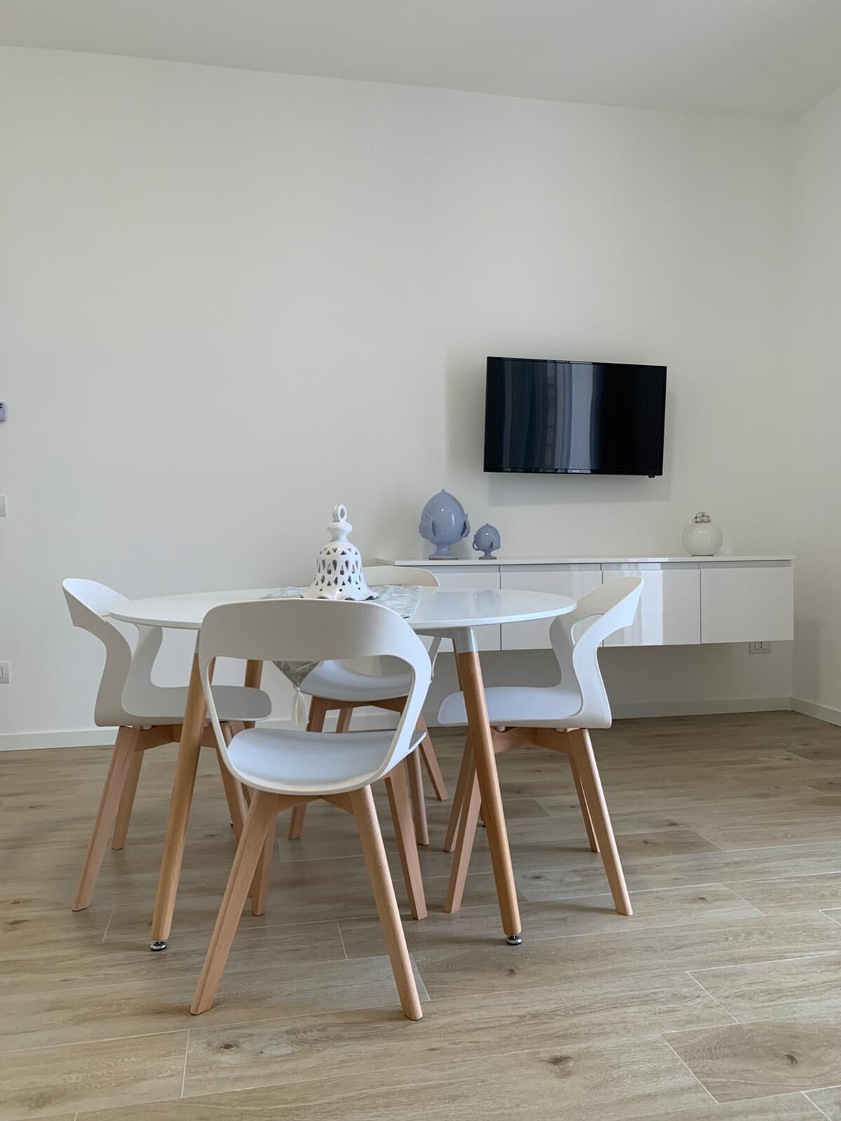 Un comedor moderno con una mesa y sillas blancas, un televisor de pantalla plana en la pared y un diseño minimalista.