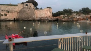 Vista de un muro de piedra histórico junto a un cuerpo de agua, con un pequeño bote y una mesa con sillas.