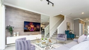A modern living room with a flat-screen TV, a glass coffee table, and a staircase. - Amazing Villa 5BR - Private Pool & Themed Rooms - 5 miles Disney! (Kissimmee)
