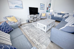 Un salon avec un canapé gris, une table basse, un téléviseur et un tapis à motifs.