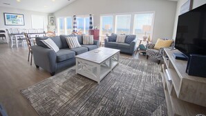 A spacious living room with two sofas, a coffee table, and a TV. There is a dining area in the background with a table and chairs. - Ocean front gem offering 6BR/5BA with direct beach access! (North Topsail Beach)