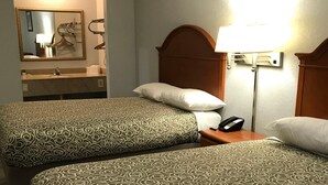 A hotel room with two beds, a bathroom with a mirror, and a bedside lamp.