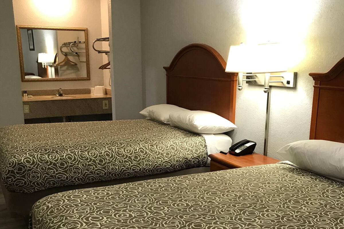 A hotel room with two beds, a bathroom with a mirror, and a bedside lamp.