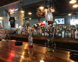 A bar area with a variety of liquor bottles, a neon sign, and a Christmas tree decoration.